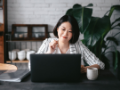 Young Asian woman having online business meeting, video conferencing on laptop with her business partners, working from home in the living room.