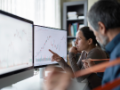 Two people looking at two screens of data